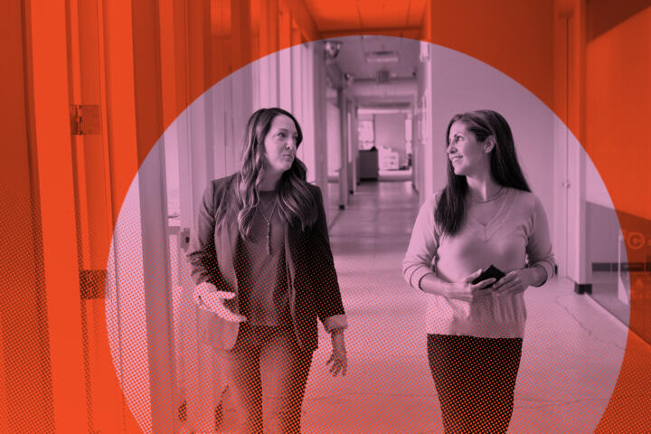 two women talk as they walk in a workplace corridor