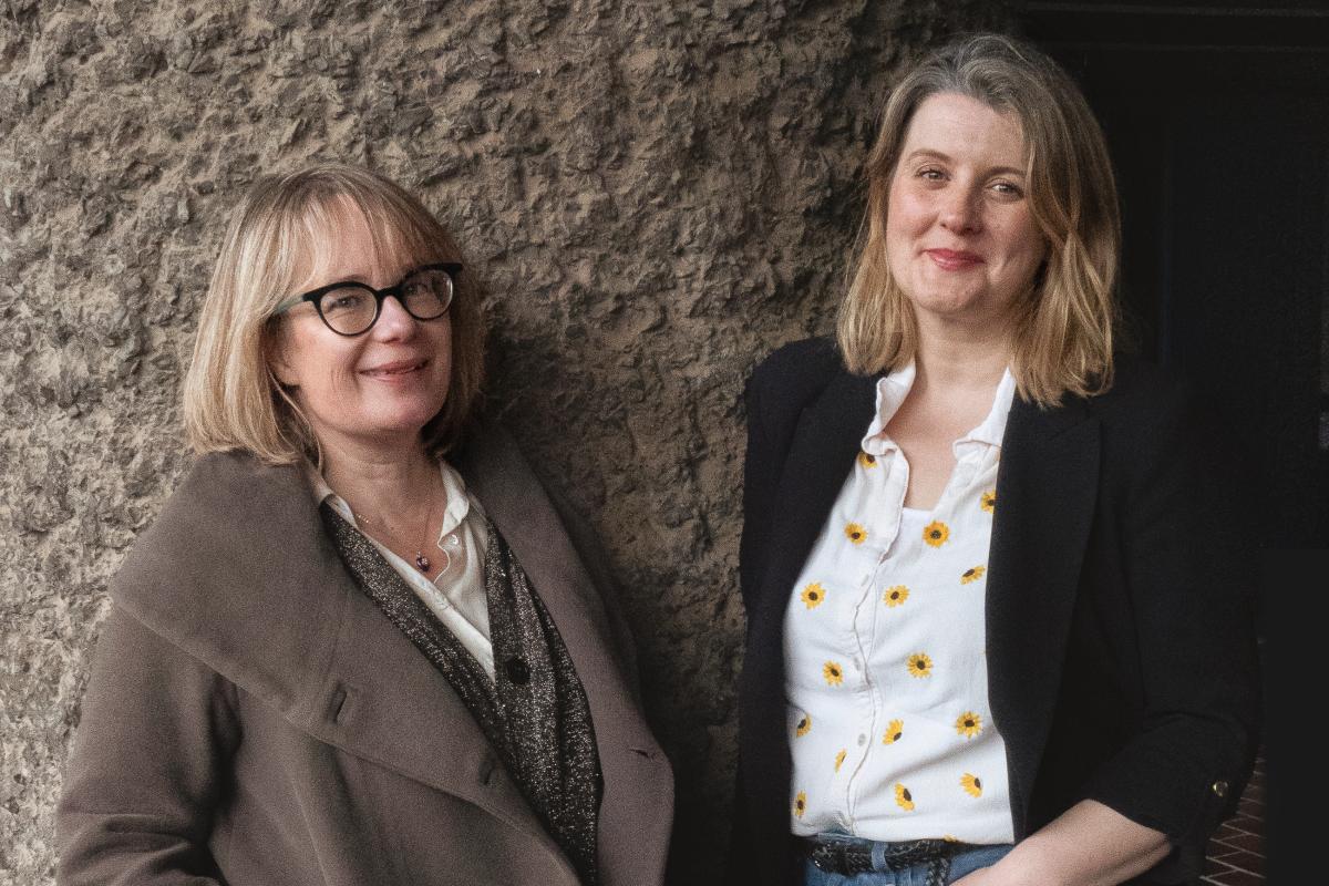 portrait of two women against a textured concrete wall